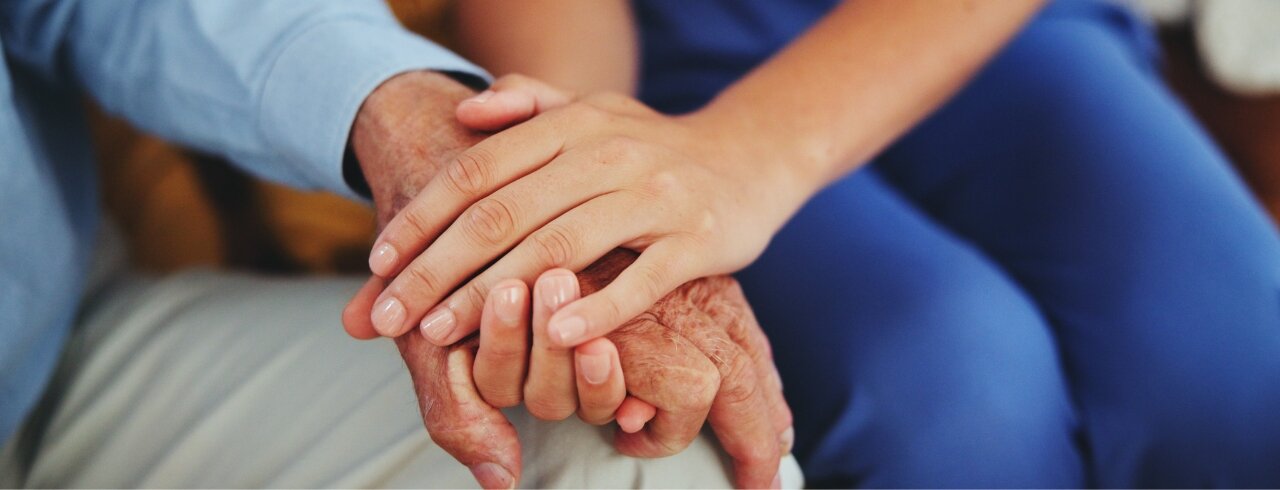 Pflegekraft hält die Hand einer älteren Person