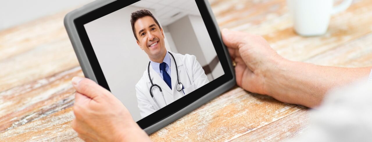 Hände halten ein Tablet in der Hand auf dem ein Arzt zu sehen ist.