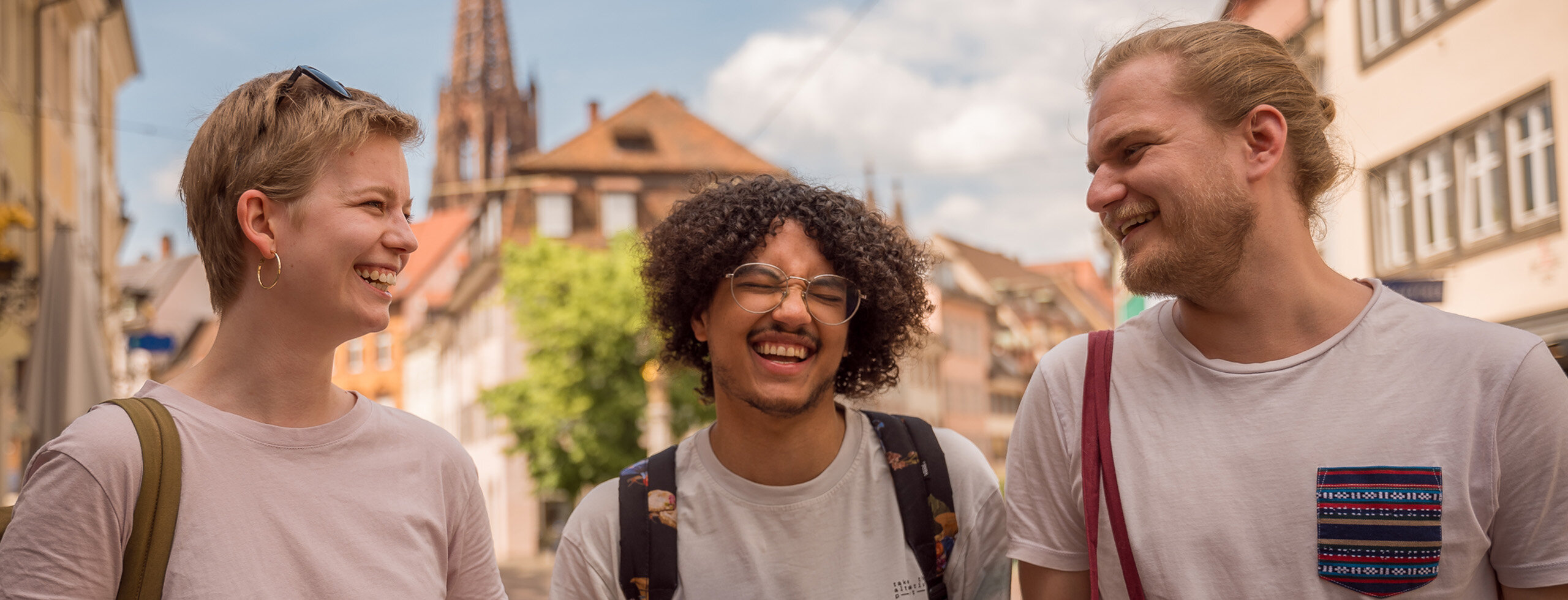 drei lachende Studierende der KH Freiburg in der Stadt mit dem Freiburger Münster im Hintergrund