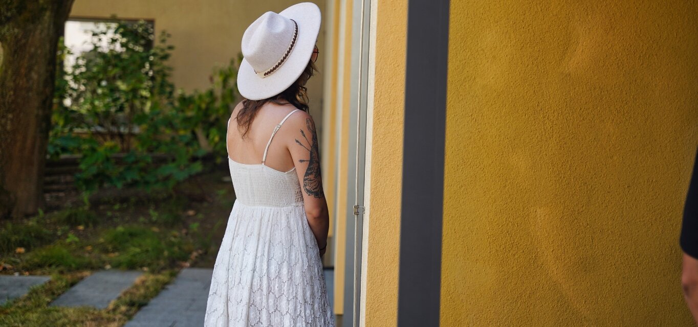 Rücken einer Person in weißem Kleid und mit weißem Hut im Hof von Campus II an der KH Freiburg
