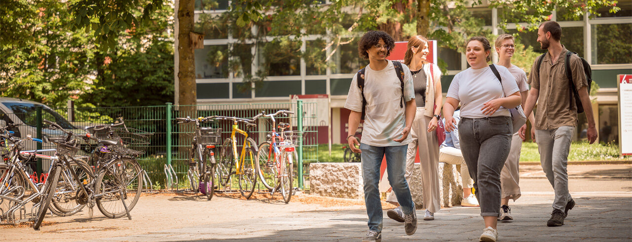 Eine Gruppe sich angeregt unterhaltender Studierender auf dem Weg von einem Gebäude am Campus I der KH Freiburg zum nächsten