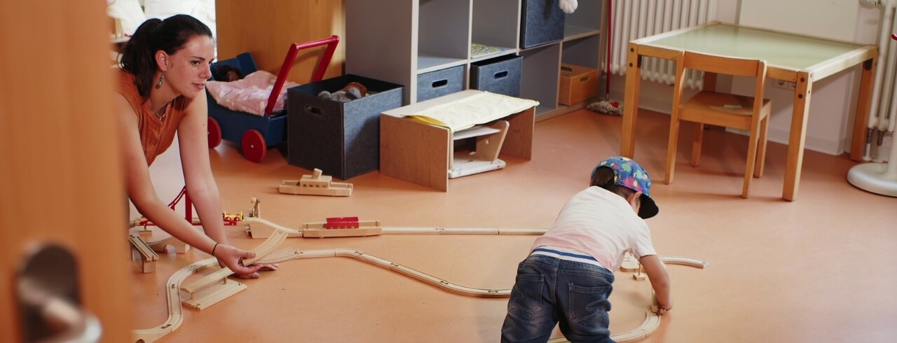 Blick in eine Situation, in der ein Kind auf dem Boden spielt und von einer Studierenden der Heilpädagogik betreut wird.