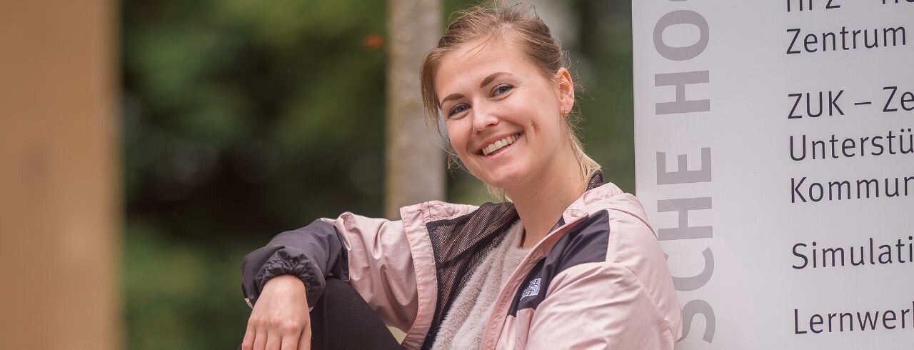 Eine Studierende der KH Freiburg sitzt lächelnd an eine Stele gelehnt