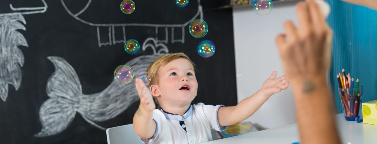 Ein Junge sitzt am Tisch und versucht Seifenblasen einzufangen