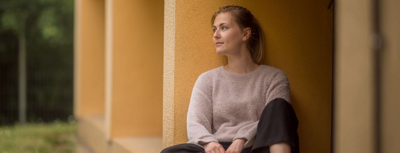 Eine Frau sitzt an die Wand gelehnt und schaut in dir Ferne