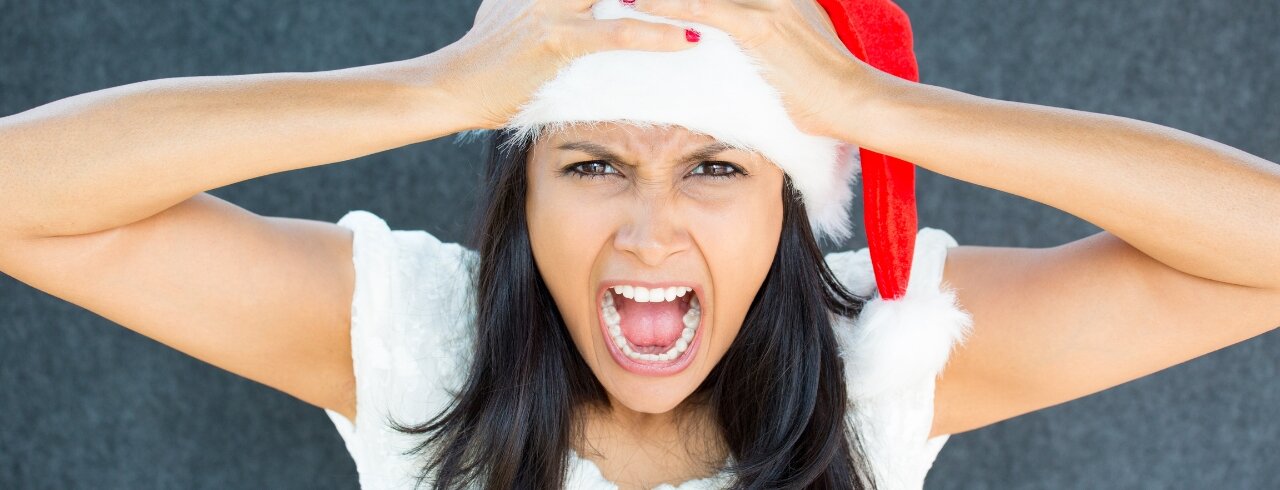 Gestresste Frau mit Weihnachtmütze auf dem Kopf, sie schlägt die Hände über den Kopf zusammen und scheint zu schreien