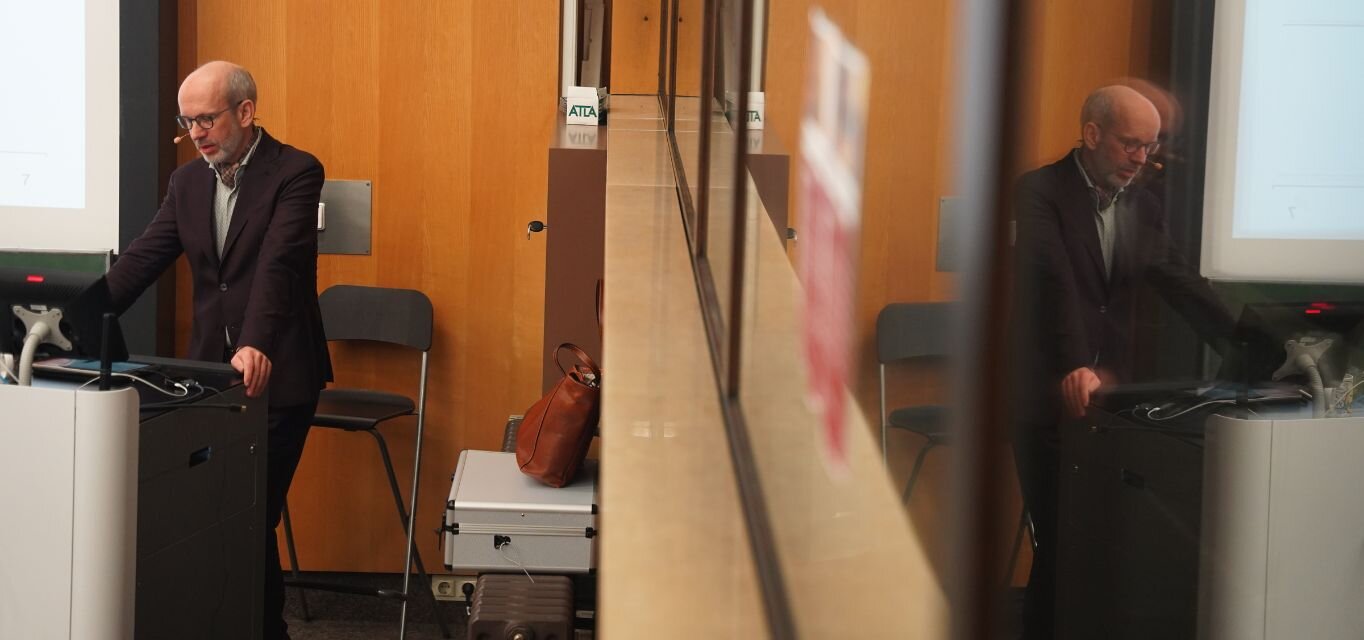 Prof. Dr. Roland Rosenow bei seinem Vortrag zur Bürgergeldreform mit Spiegelung im Fenster der Aula