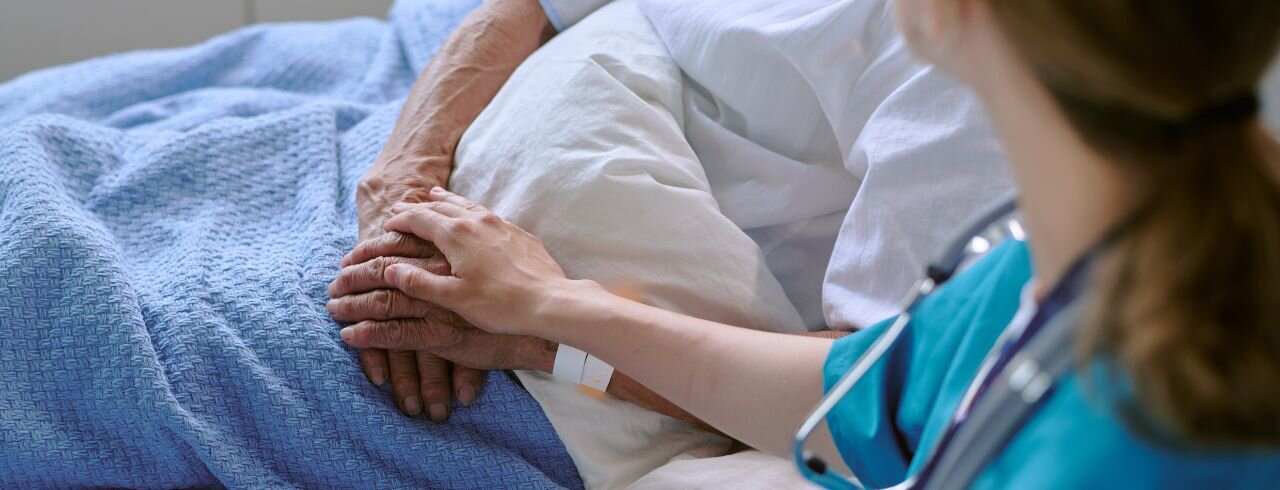 Pflegekraft hält die Hand einer älteren Person als Zeichen von Unterstützung.